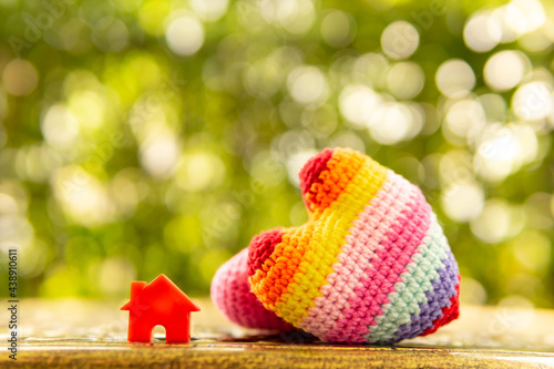 Hand are hold rainbow heart and home model.Give love to the family for happiness..Have background in garden and light of sun.