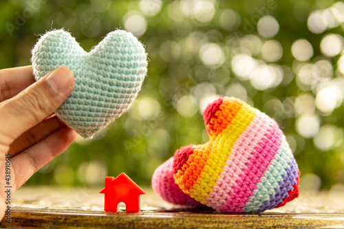 Hand are hold rainbow heart and home model.Give love to the family for happiness..Have background in garden and light of sun.