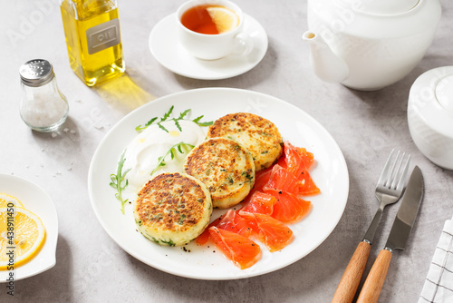 Salted cottage cheese pancake with greens, served with smoked salmon slices and sour cream. Healthy breakfast. Light gray background.