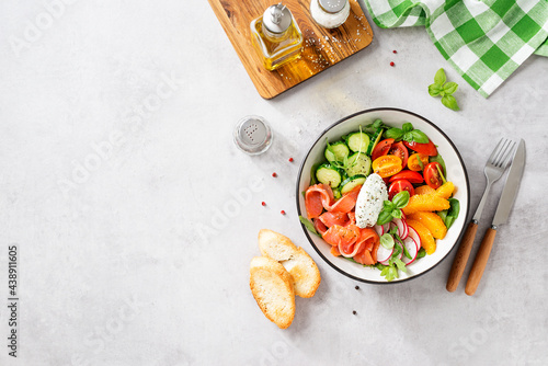 Salmon bowl with spinach,arugula, cherry tomatoes, cucumber, orange slices, radish and cream cheese. Homemade food. Concept for a tasty and healthy meal. Light gray stone background. Top view. 