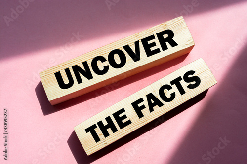 Uncover the facts word on wooden blocks on pink background. Fake or real news business concept. photo