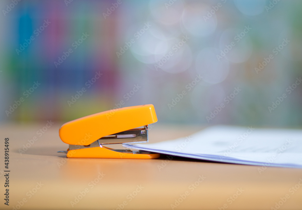 An orange stapler that sits on the desk ready for stapling the papers ...