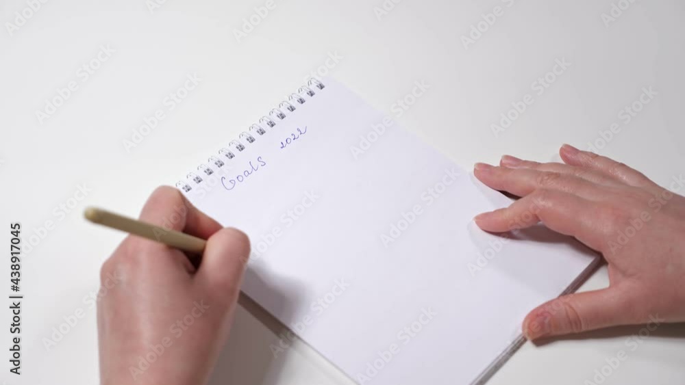 Close-up of female hands writing with left hand the goals for 2022. Close-up of female hands writing with left hand the goals for 2022.