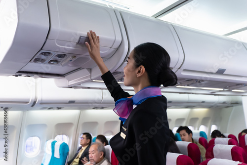 Young beautiful Asian airline cabin crew attendant closing overhead cabinet luggage compartment for checking safety of passenger before flight. Airline business professional uniform occupation concept photo