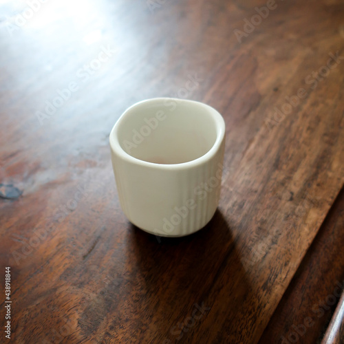 Empty vintage cup on a traditional wooden table background, sunny morning atmosphere with incoming light shining on the cup.