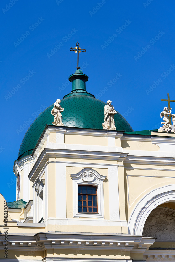 Green dome with a cross and a roof with sculptures against the blue sky