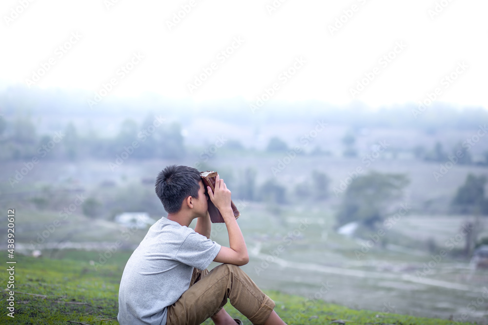 Boy sitting praying on the green fields with a Bible, Focus face, Children's beliefs of christian concept. Boy sitting praying on the green fields with a Bible, Focus face, Children's beliefs of christian concept.