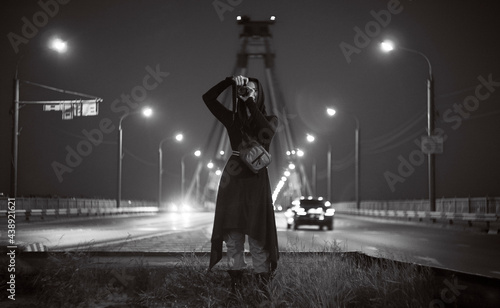 Young woman in black mantle with a camera shooting night street