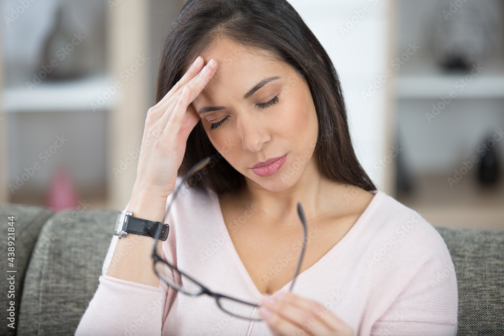 woman holding eyeglasses and rubbing her head woman holding eyeglasses and rubbing her head