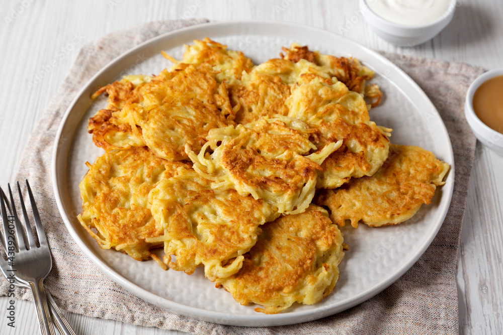 Homemade Potato Pancakes Latkes with Apple Sauce and Sour Cream on a white wooden surface, side view. Close-up. Homemade Potato Pancakes Latkes with Apple Sauce and Sour Cream on a white wooden surface, side view. Close-up.
