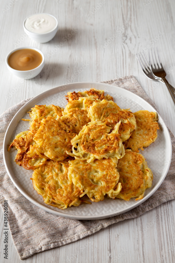 Homemade Potato Pancakes Latkes with Apple Sauce and Sour Cream on a white wooden background, side view.