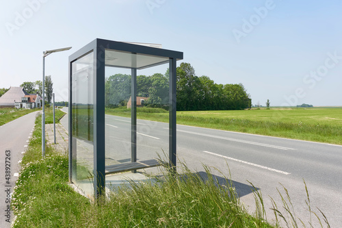 Fototapeta Naklejka Na Ścianę i Meble -  Bus stop shelter with glass on a road in a rural area under a blue sky.