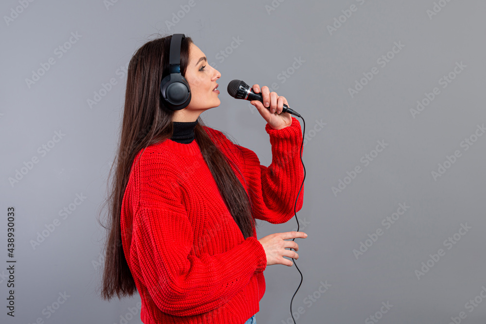 Obraz premium young, emotional brunette with headphones and a microphone dressed in a red sweater sings karaoke