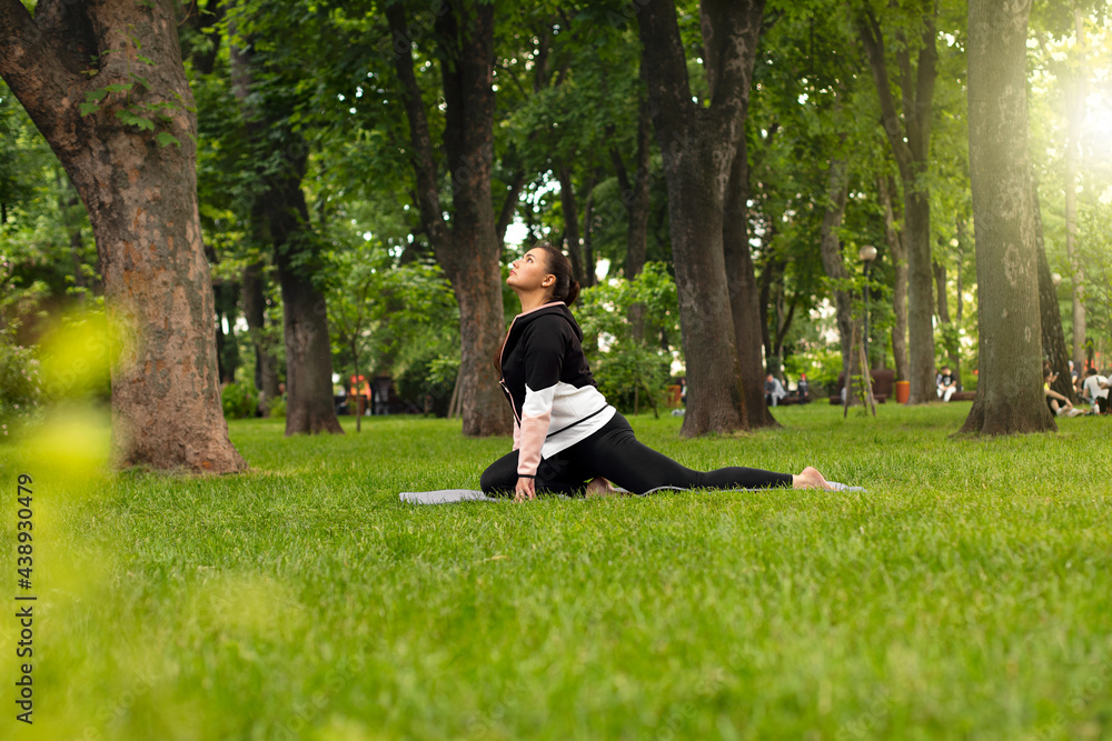 woman doing sports, shows exercise from pilates. practices yoga in the park on the green grass.