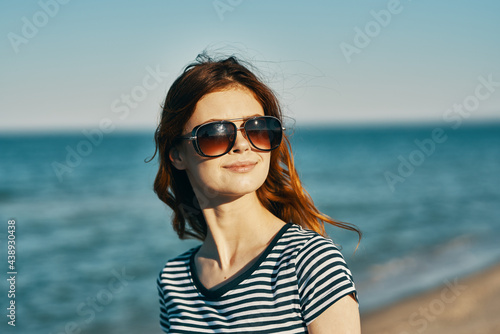 a woman in a t-shirt and glasses walks along the sandy shore on the beach near the blue sea © SHOTPRIME STUDIO