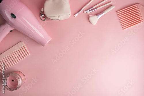 Woman accessories on pink background. Hairdryer, comb, cosmetic brushes, cosmetic bag over pink background with copy space.

