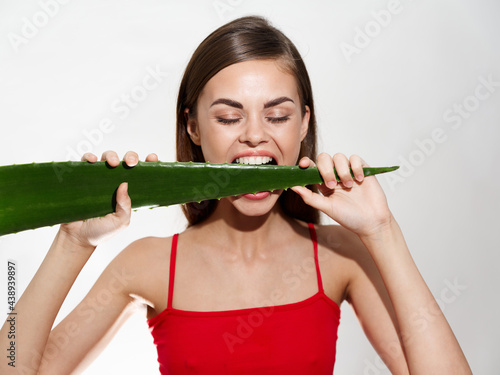 emotional woman with white teeth gnaws an aloe leaf on a light background