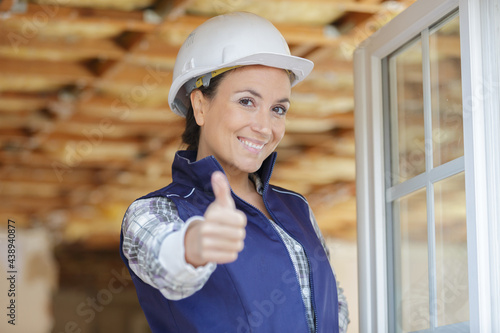 female builder at open window holding thumbs up