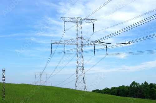 High voltage eletrical towers and lines with blue sky and green meadow. Eletricity towers on a green field. High-voltage transmission lines. Electricity transmission towers. photo