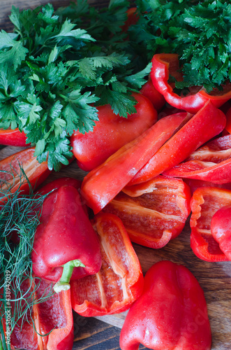 Raw red bell pepper, chopped in half and parsley on a wooden background.