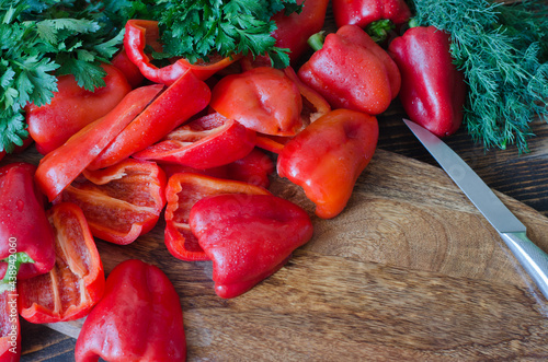 Raw red bell pepper, chopped in half and parsley on a wooden background.