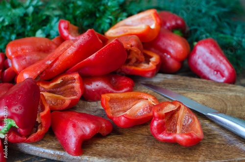 Raw red bell pepper, chopped in half and parsley on a wooden background.