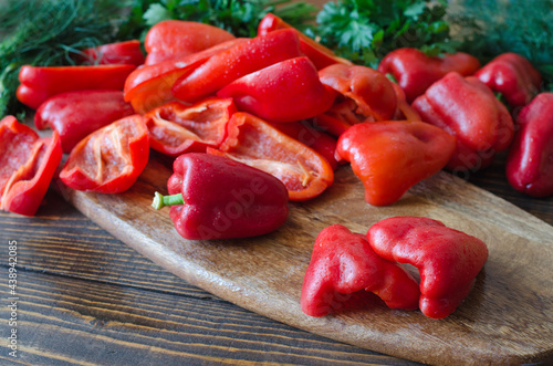 Raw red bell pepper, chopped in half and parsley on a wooden background.