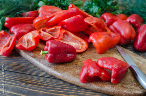 Raw red bell pepper, chopped in half and parsley on a wooden background.
