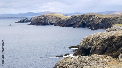 A static shot of the rugged coastal  cliffs making up the coastline on Kenna Ness on the west side of Mainland, Shetland, UK. Waves break on the rocks at the foot of the high cliffs. photo