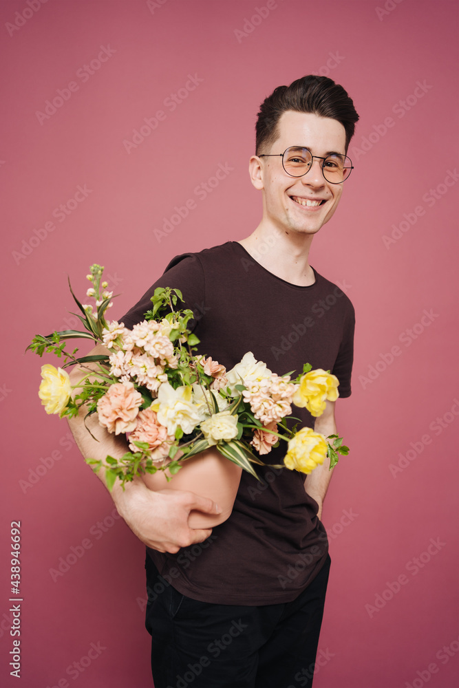 A young man is holding a beautiful bouquet of flowers in his hands on a pink background. The guy decided to make a surprise to his girlfriend. Mother's Day. Women's day. Flowers delivery. A young man is holding a beautiful bouquet of flowers in his hands on a pink background. The guy decided to make a surprise to his girlfriend. Mother's Day. Women's day. Flowers delivery.