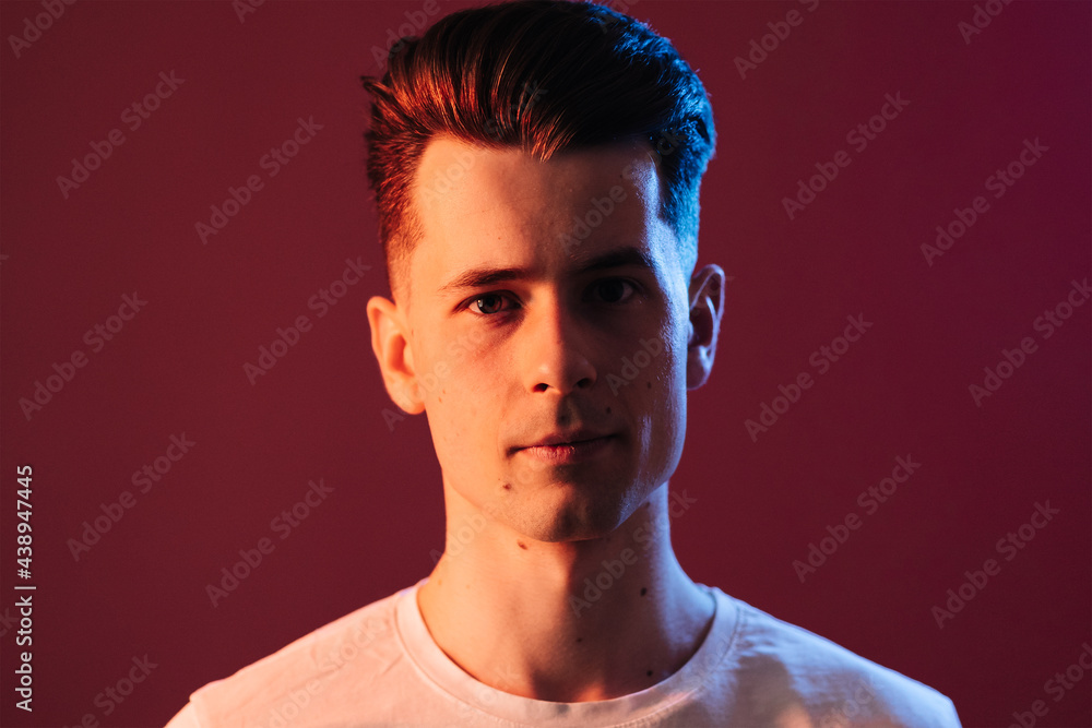 Obraz premium Isolated shot of young serious handsome male with trendy hairdo, wears casual brown t shirt, has serious expression as listens to interlocutor, poses in studio against crimson background