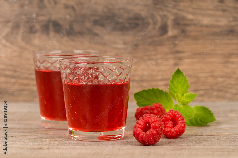 homemade sweet raspberry wine or juice in small glasses with fresh berries on aged wooden table