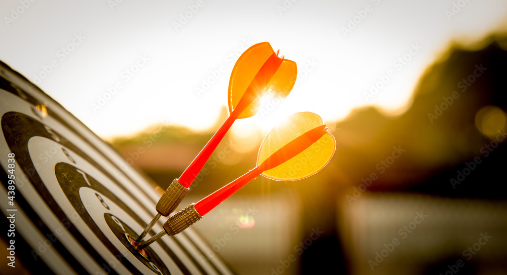 Close up shot red darts arrows in the target of dartboard center on dark blue sky background. Business target or goal success and winner concept. Close up shot red darts arrows in the target of dartboard center on dark blue sky background. Business target or goal success and winner concept.