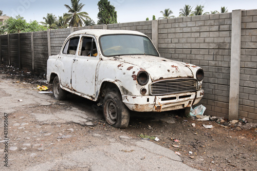 An Old abandoned car of Indian make in dilapidated condition with lots of rust and missing parts seen on an empty street.