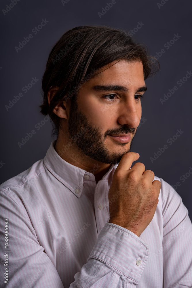 Portrait of Attractive Hispanic Man with beard and Long Hair Dressed in Shirt with Thoughtful Gesture of Hand on Chin Isolated on Gray Background