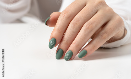 Hands of a young woman with green olive matte nails on a light gray background. Manicure, pedicure beauty salon concept. Copy space for text or logo. Gel polish and abstract white spider web pattern