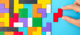 Hand connecting colorful wood puzzle pieces on blue background, geometric shape block. Concepts of logical thinking, Conundrum, solutions, rational, strategy, world logic day and Education