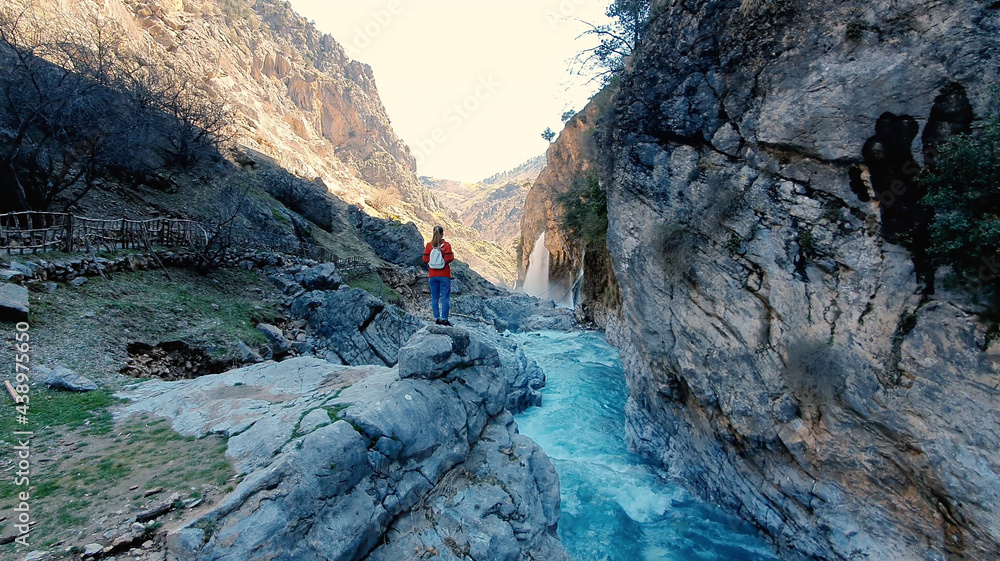 Woman looking on huge waterfall. Traveler rising her hands near waterfall