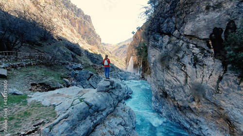 Woman looking on huge waterfall. Traveler rising her hands near waterfall