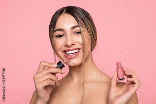 Sexy woman lips with pink makeup and gloss  closeup of a young dark-skinned woman applying lipgloss with brush on a white background