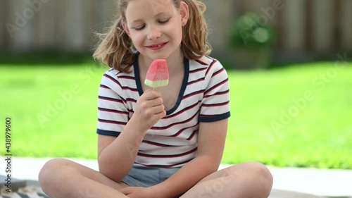 Happy little teen girl lick refreshing ice cream  and joying sunny summer time at green backyard photo