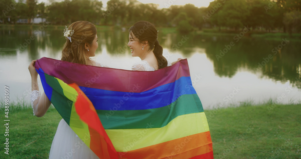 Portrait Of Asian Lesbian Couple With LGBT Flag Walking Together In The Park. Two Happy Girlfriends Pose With Rainbow Flag.
