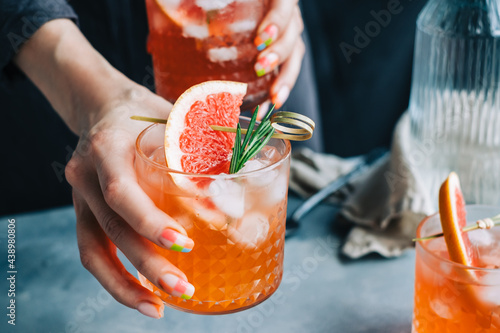 Female bartender hand holding grapefruit cocktail lemonade glasses  with ice and rosemary. photo