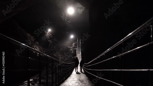 Two female figures walk in a huge underground cave on a suspension bridge Abhazia photo