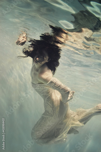A girl in a long dress with sequins flies under water as if in weightlessness