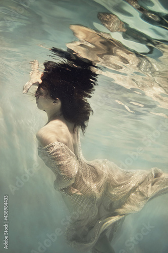 A girl in a long dress with sequins flies under water as if in weightlessness