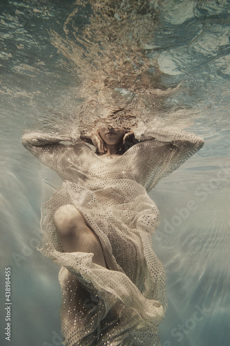 A girl in a long dress with sequins flies under water as if in weightlessness