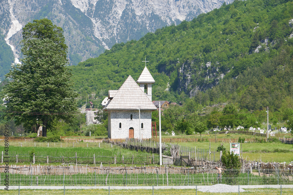 Village church in the Theth Valley with snow capped mountains in the background, in Albania.