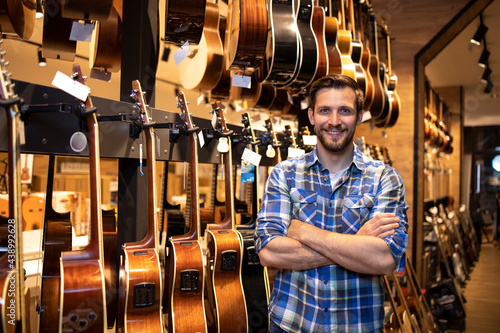 Portrait of professional seller standing in music shop and selling guitars instruments.