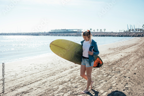 Young girl walking along the shore with surfboard. Vacation concept.